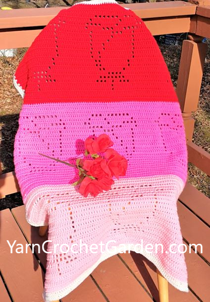Filet crochet rose blanket pattern in red, hot pink, and light pink draped over an outdoor wooden chair