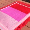 Overhead flat lay of filet crochet rose blanket in red, hot pink, and light pink on a wooden deck surrounded by red roses