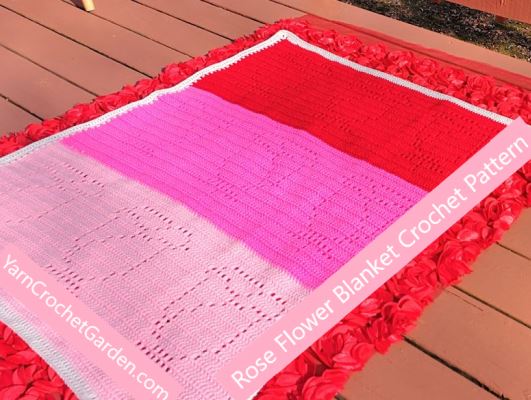 Overhead flat lay of filet crochet rose blanket in red, hot pink, and light pink on a wooden deck surrounded by red roses
