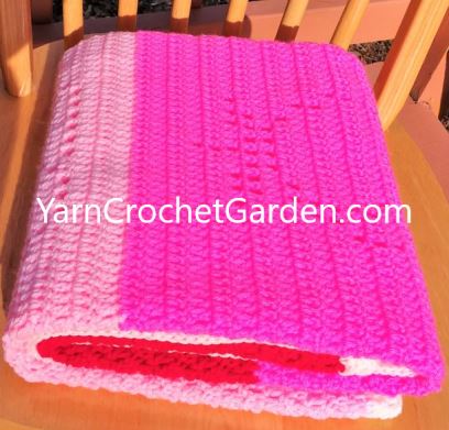 Folded filet crochet rose blanket in hot pink and light pink yarn on a wooden chair