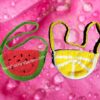 Two handmade crochet purses, one shaped like a slice of lemon and the other like a watermelon wedge, sitting on a wooden table.