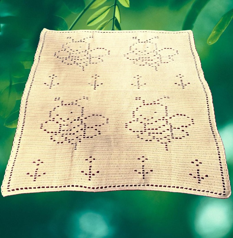 Finished filet crochet bee blanket displayed on a soft surface
